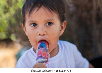 A Young Latino Boy Eating A Frozen Ice Treat And With A Look Of Surprise On His Face.