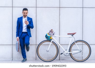 Young Latino Businessman Using Cellphone While Holding His Bike. Latino Business Man Using Mobile Phone Outdoors. Business Concept.