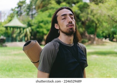 Young, Latino, Hispanic hippie male with long hair breathing deeply in a natural environment with a gazebo behind him.
