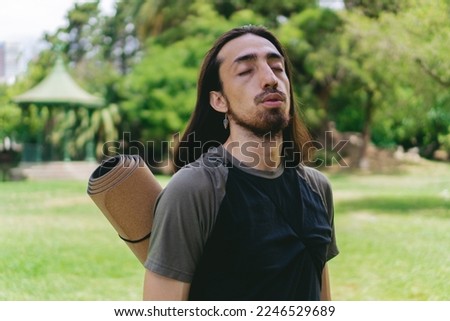 Young, Latino, Hispanic hippie male with long hair breathing deeply in a natural environment with a gazebo behind him.
