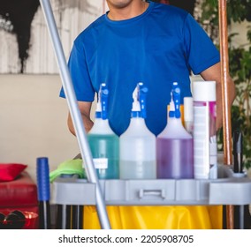 Young Latino Janitorial Worker In Blue Uniform And Trolley With Tools And Cleaning Supplies (sprayers, Broom, Cleaners, Etc)