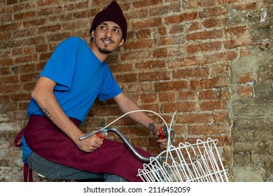 Young Latino Male (28) Riding A Bicycle With Basket On His Way To Work. Copy Space, Brick Background. Concept Jobs