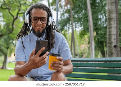 Young Latino man with dreadlocks using a smartphone on a park bench