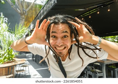 young latino man with dreadlocks of venezuelan ethnicity, he is desperate with his hands on his head and with a funny face, standing in front of a restaurant