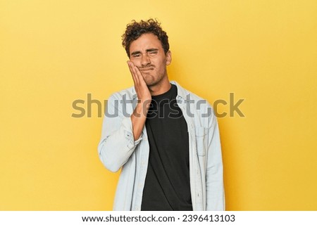 Young Latino man posing on yellow background having a strong teeth pain, molar ache.