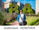 Young Latino man smiling and walking near green sculptures in Buenos Aires, Argentina, enjoying a sunny day.