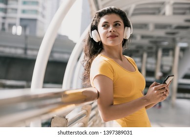 Young Latino Woman Wearing Bluetooth Headphones Listening To Music In The City