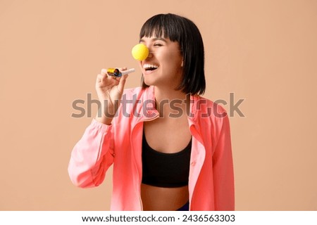 Young laughing female fitness trainer with party blower on beige background. Fool's day