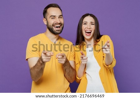 Young laughing happy joyful cool fun couple two friends family man woman together in yellow casual clothes point index finger camera on you joking isolated on plain violet background studio portrait