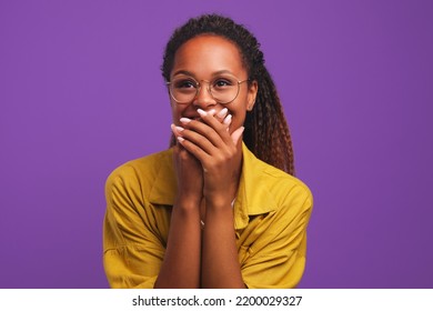 Young laughing pretty girl African American woman covers mouth with hands tries to hide joy or laughter after hearing joke dressed in yellow shirt stands in purple solid background - Shutterstock ID 2200029327
