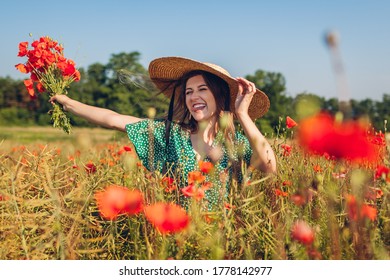 Young Laughing Woman Raised Arm Holding Bouquet Of Poppies Flowers Walking In Summer Field. Happy Woman Feeling Free