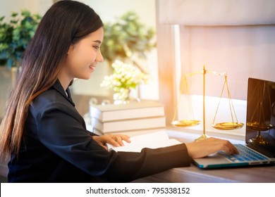 Young Lawyer Woman Work On Laptop With Scale Of Justice And Law Textbook On Table In Office, Feel Happiness When Prepare An Advice For Courtroom. Notary Student Study On Legal Law. Layer Concept.
