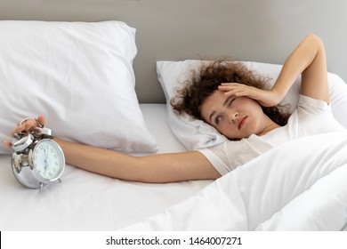 Young Lazy Woman Putting Her Alarm Clock Off On The Bed In Bedroom