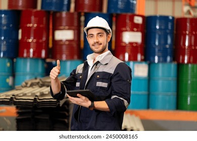 Young leader worker showing thumb up with tablet in hand, wear helmet for safety during working in Metal Lathe heavy factory with storing industrial lubricants. Hazardous Material Storage background - Powered by Shutterstock