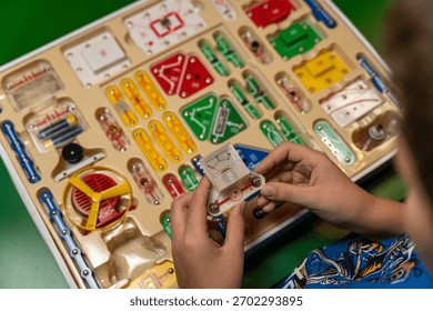 Young learner is actively exploring electronic circuit kit, manipulating colorful components and connections, encouraging creativity and critical thinking in an engaging atmosphere