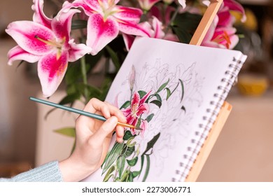 Young left-handed girl painting still life with flowers, purple lilies, with watercolor paints on the easel at home - Powered by Shutterstock