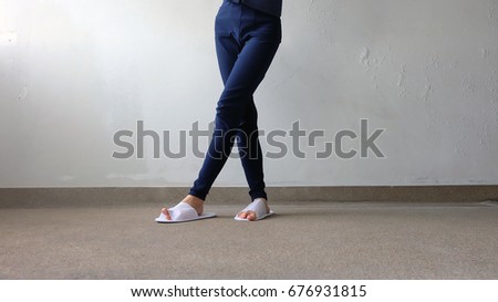 Young Female’s Legs and Feet Wearing White Slippers and Blue Pants on Ground, Indoor Background Great For Any Use.