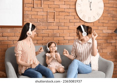 Young lesbian couple with adopted little girl in headphones listening to music at home - Shutterstock ID 2365081937