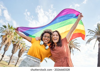 Young Lesbian Couple Celebrates Pride Day Looking At Camera With Rainbow Flag. Concept Of Homosexuality, Gay.