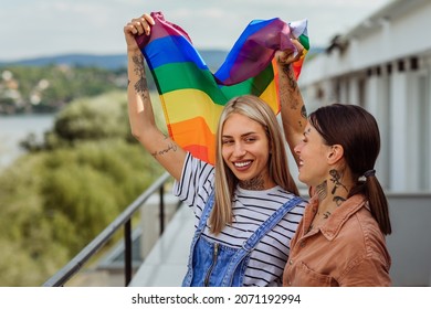 Young lesbian couple celebrating their love. They are hugging and smiling while holding rainbow flag - Powered by Shutterstock