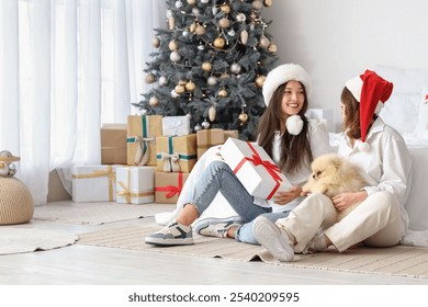 Young lesbian couple with dog and gift in bedroom on Christmas eve - Powered by Shutterstock