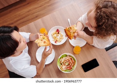 Young Lesbian Couple Eating Pizza Slices With Homemade Salad When Having Dinner At Home, View From The Top