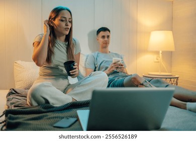 Young lesbian couple relaxing in bed, sipping coffee and watching a movie on their laptop, enjoying a cozy evening together filled with warmth and intimacy in their apartment - Powered by Shutterstock