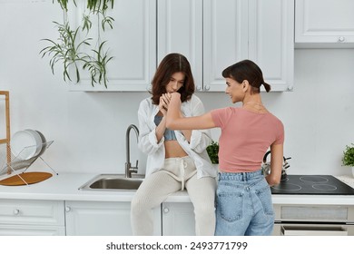 A young lesbian couple share a tender moment in their kitchen, one woman kissing the others hand. - Powered by Shutterstock