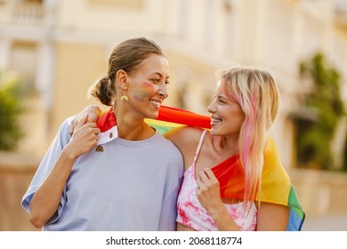 Young lesbian couple standing with rainbow flag during pride parade on a street street - Shutterstock ID 2068118774