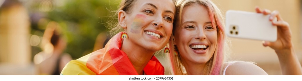 Young Lesbian Couple Taking Selfie On Cellphone During Pride Parade Outdoors