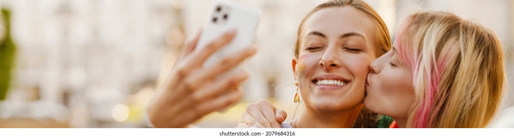 Young Lesbian Couple Taking Selfie On Cellphone During Pride Parade Outdoors