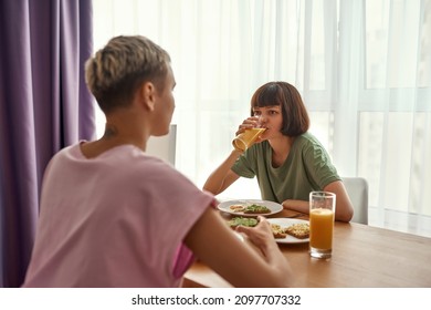 Young lesbian european couple having breakfast at table at home. Concept of domestic lifestyle. Idea of homosexual relationship and spending time together. Modern apartment. Sunny morning time - Powered by Shutterstock