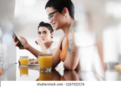 Young Lesbian Woman Gets Mad And Jealous Of Her Girlfriend, Partner Using A Smartphone And Not Paying Attention To Her. The Woman Is In A Bad Mood Because Friend Spends Too Much Time In Social Media