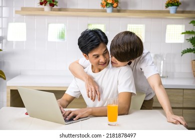 Young LGBT Asian Gay Man Hug His Partner Who Work On Laptop Computer From Behind. Happy Couple Together At Home. Same Sex Family.