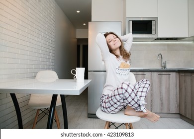 Young light brown woman in pajamas sitting on chair with white cup and catch up in white kitchen at morning - Shutterstock ID 423109813