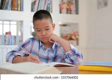 Young Little Asian Kid Boy Schoolboy Writing Drawing On Notebook. Child Children Doing Homework. Childhood Education