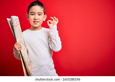 Young Little Boy Kid Looking At Turist City Destination Map Over Red Isolated Background Doing Ok Sign With Fingers, Excellent Symbol