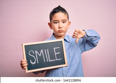 Young Little Boy Kid Showing Blackboard With Smile Word As Happy Message Over Pink Background With Angry Face, Negative Sign Showing Dislike With Thumbs Down, Rejection Concept