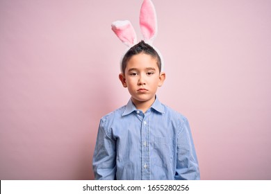 Young little boy kid wearing easter bunny ears over isolated pink background with serious expression on face. Simple and natural looking at the camera.