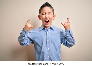 Young little boy kid wearing elegant shirt standing over isolated background shouting with crazy expression doing rock symbol with hands up. Music star. Heavy concept.