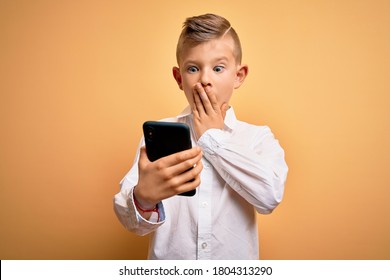 Young Little Caucasian Kid Using Smartphone And Looking At The Screen Of The Phone Cover Mouth With Hand Shocked With Shame For Mistake, Expression Of Fear, Scared In Silence, Secret Concept