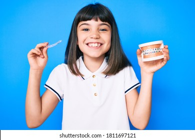Young little girl with bang holding invisible aligner orthodontic and braces smiling with a happy and cool smile on face. showing teeth. 