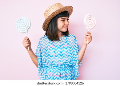 Young Little Girl With Bang Wearing Summer Dress Eating Candy Smiling Looking To The Side And Staring Away Thinking. 