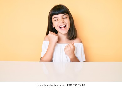 Young Little Girl With Bang Wearing Casual Clothes Sitting On The Table Celebrating Surprised And Amazed For Success With Arms Raised And Eyes Closed 