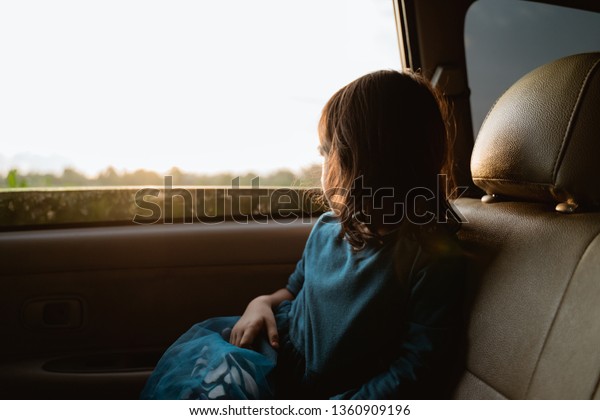 young little girl enjoying the trip in back\
seat looking out the window of the\
car