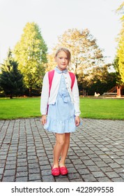 A Young Little Girl Preparing To Walk To School, Wearing Blue Mary Jane Dress And Red Moccasins