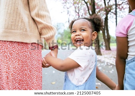 Young little girl walking with her mother and sister in the garden with a bright smile. Concept parents teach walking and travel in nature. Funny
