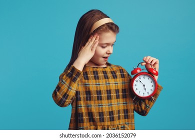 Young Little Kid Looking Shocked At Classic Bell Alarm Clock Over Isolated Yellow Background, Stressed For Mistake, Expression Of Fear