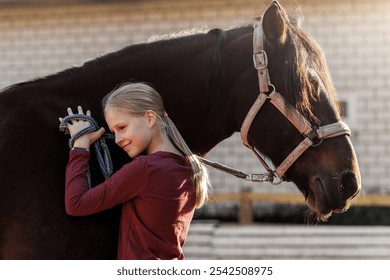 Young little teenager kid girl portrait hugging chestnut horse  at stable ranch yard. Horse riding school exercise. Cute little beginner blond girl near beautiful brown pet. Equine hobby therapy - Powered by Shutterstock