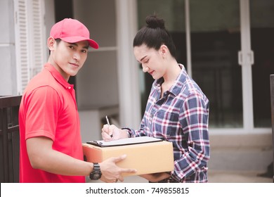 Young Logistic Career Concept. Happy Delivery Man Giving His Package To Customer At Home. Taken In Real House. Asian Chinese Fit Man In Red Polo Shirt And Jeans With Red Hat In His Early Twenties.